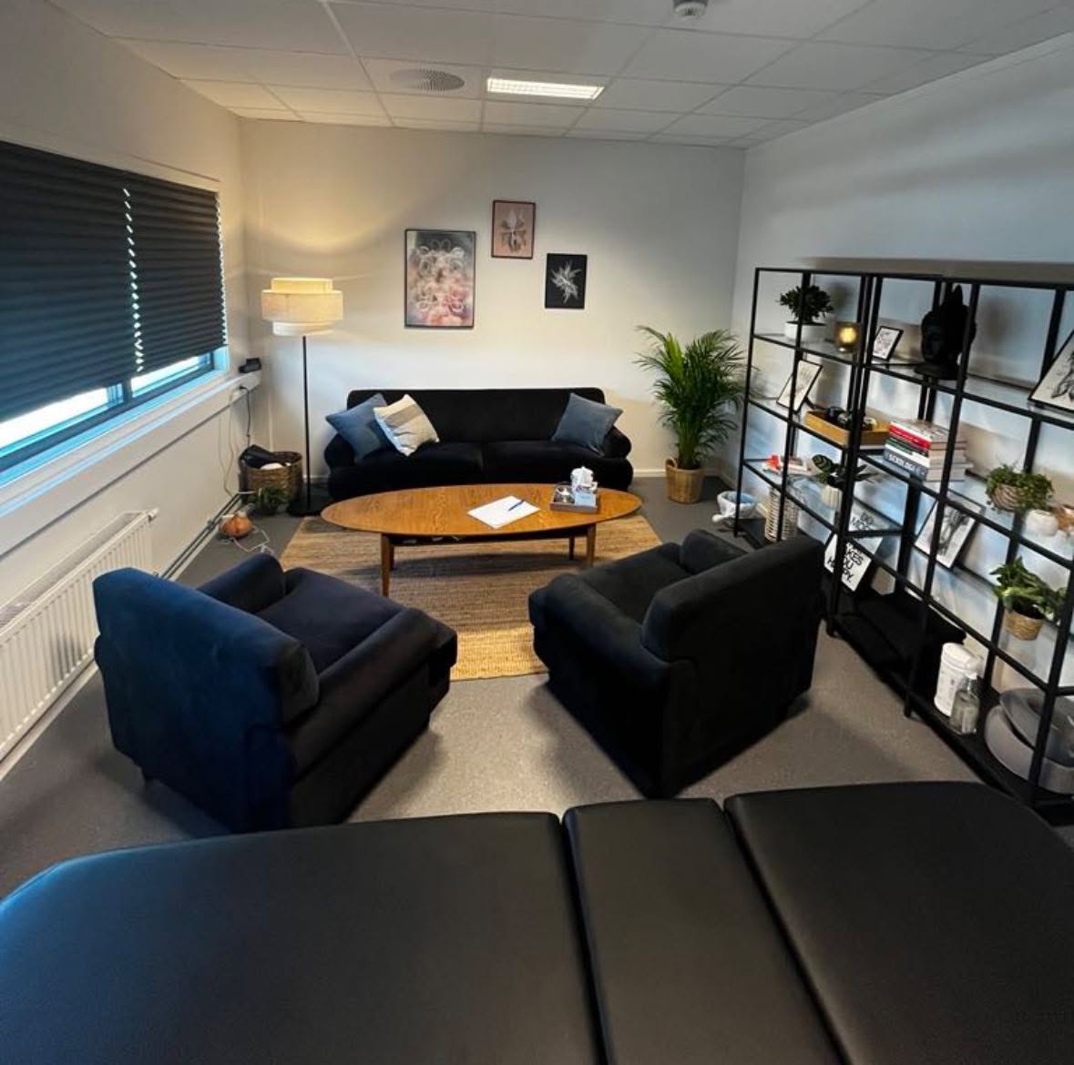 Terapirom hos SansHera Helhetsterapi på Jessheim, en sort sofa, et salongbord med servert vann, to sorte stoler