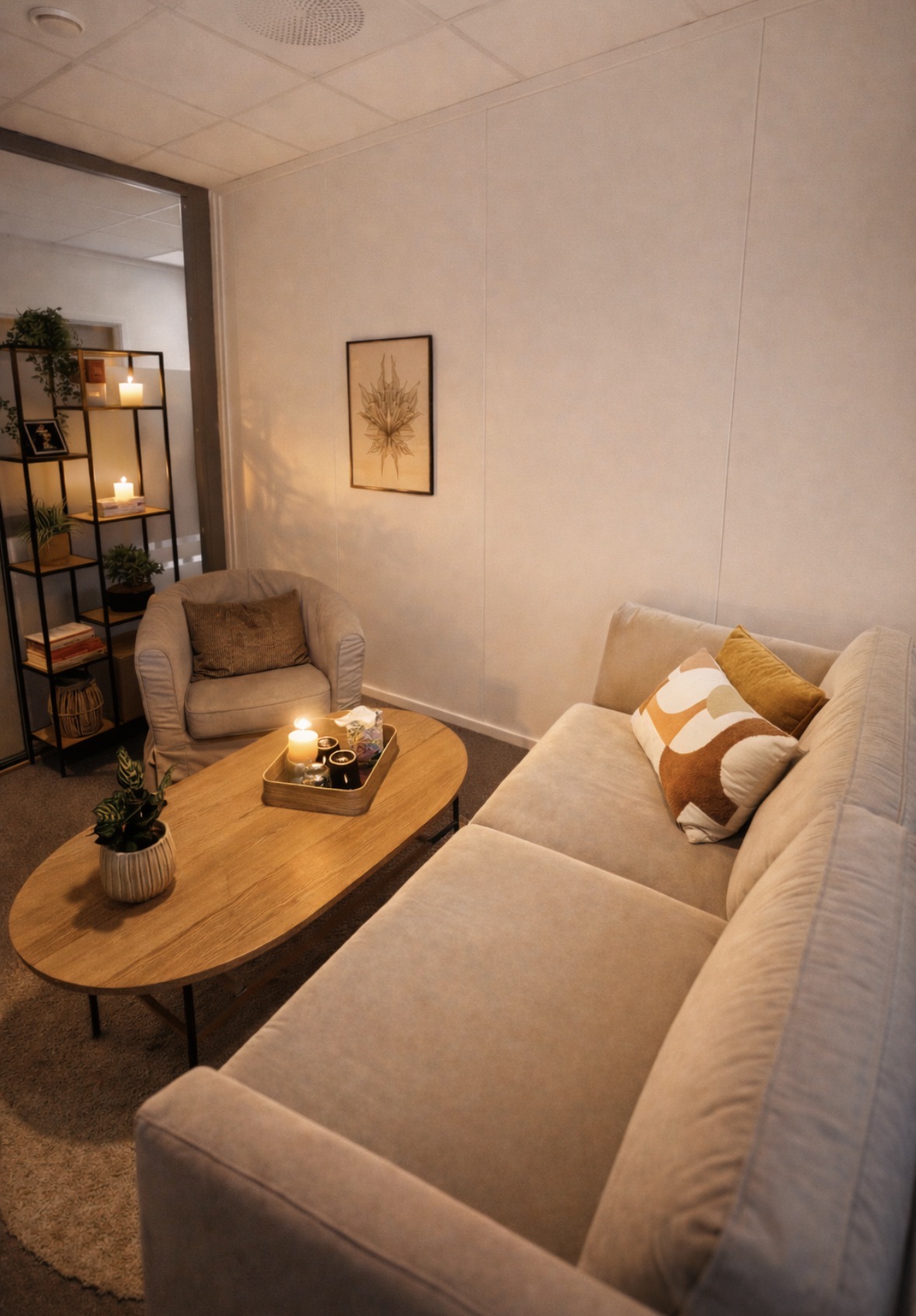 Terapirom hos SansHera Helhetsterapi på Jessheim, en beige sofa og en beige stol, et salongbord dekorert med en plante og et pyntebrett med lys og drikke på, koselig og trygt rom